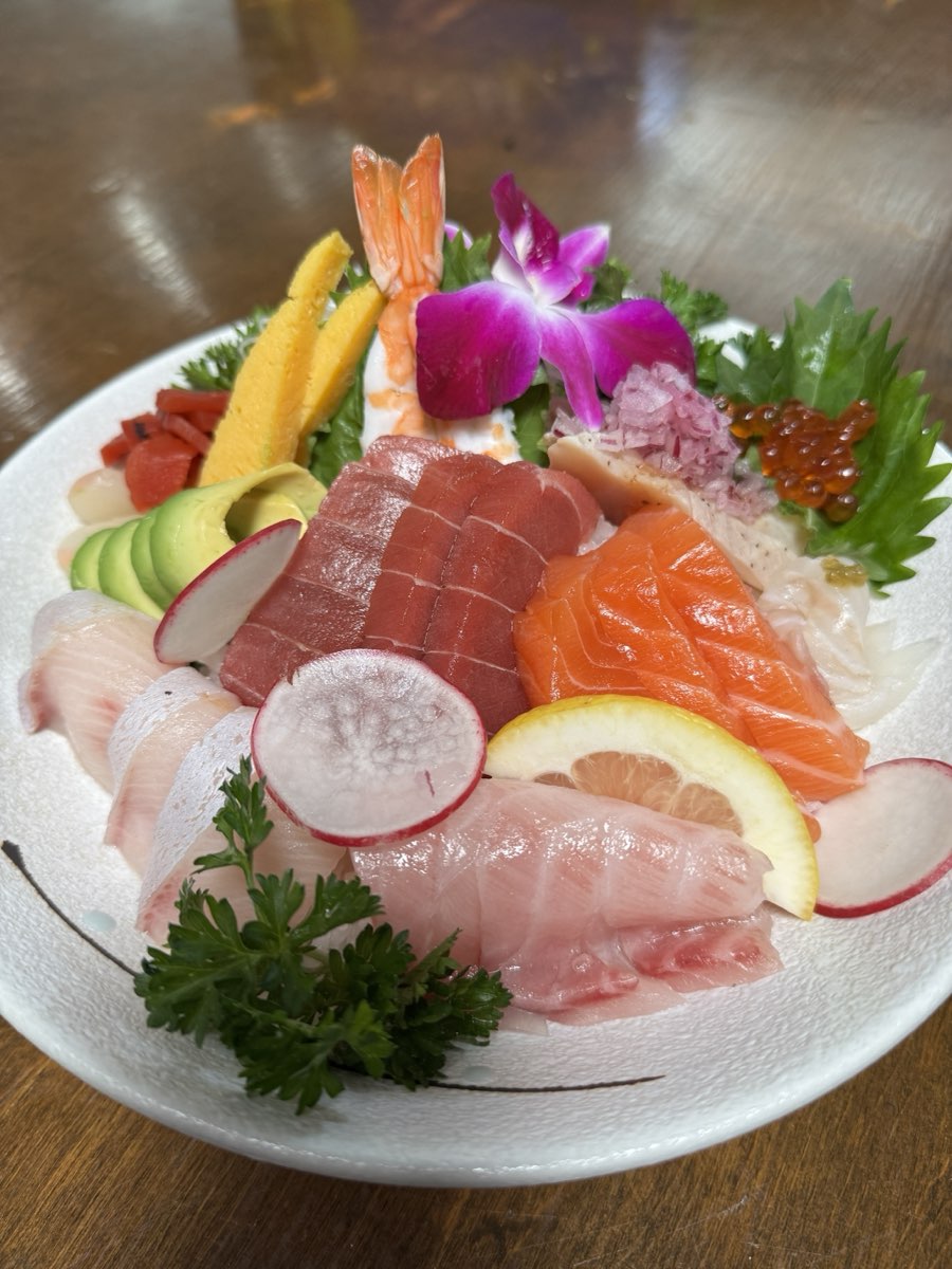 A chirashi bowl of assorted sashimi over rice: tuna, salmon, yellowtail, shrimp, avocado, and salmon roe