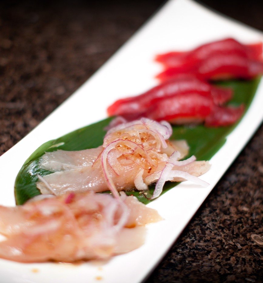 A long white plate of tuna and white fish, dressed with shaved onion and ponzu